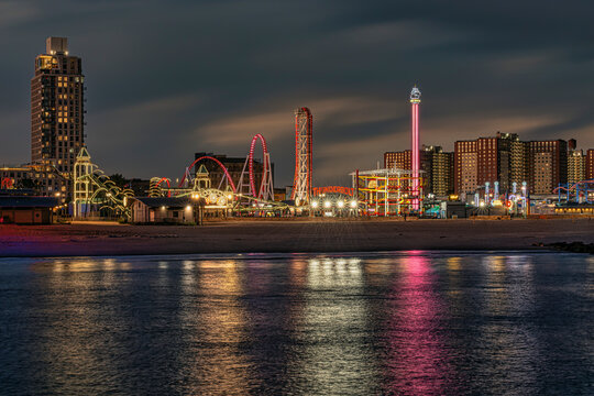 Amusement park Coney Island rides illuminated at night with reflections in calm water. New York, USA