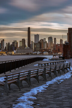 Empty benches overlooking the city skyline with snow and dramatic clouds at sunset. New York, USA