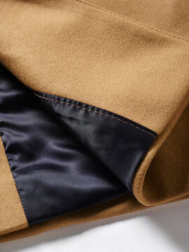 A close-up of a beige coat with a smooth black satin lining on a light surface.
