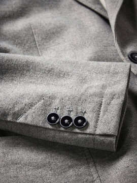 Gray blazer sleeve with three unique black buttons and a neatly stitched pocket.