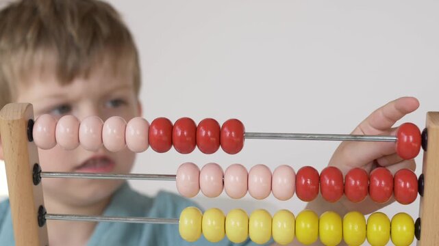 Close-up view of child moving colorful abacus beads while learning arithmetic. Educational footage showing number recognition, counting practice and early mathematics development. Boy studies abacus