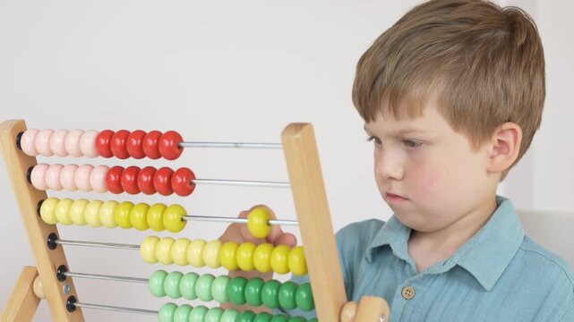 Little boy concentrates while moving colorful beads on wooden abacus during early mathematics lesson at home. Educational activity develops counting skills, logical thinking, problem solving abilities