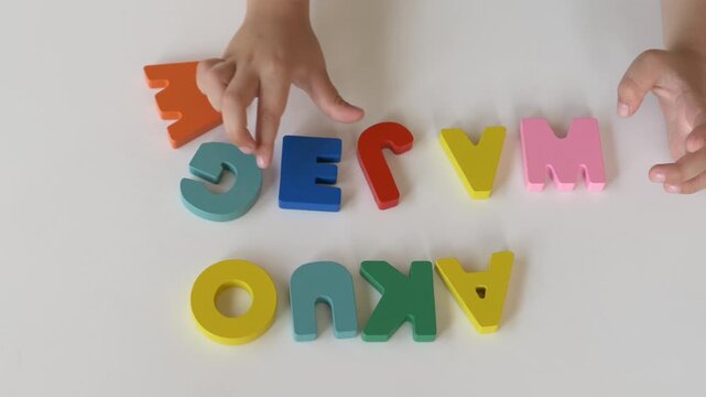 Hands arranging wooden alphabet pieces on learning board. Educational footage about preschool education, reading preparation and cognitive growth. Child places alphabet letters into correct positions