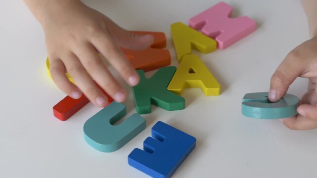 Hands of young child sorting alphabet puzzle pieces during educational play. Concept of preschool education, reading preparation and cognitive development.