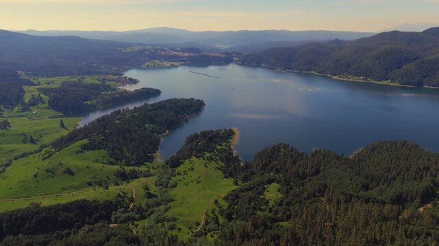 High altitude drone panorama overlooking the expansive blue waters of Dospat Reservoir surrounded by lush green forests and valleys in Bulgaria