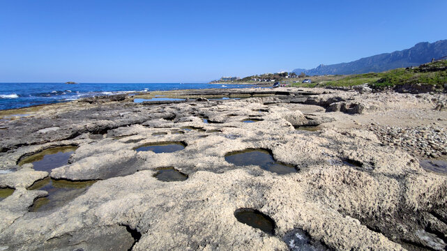 Scenic view of the ancient rock-cut Queens Bath pools along the rocky coastline of Lapta, Cyprus, under a clear blue sky.
