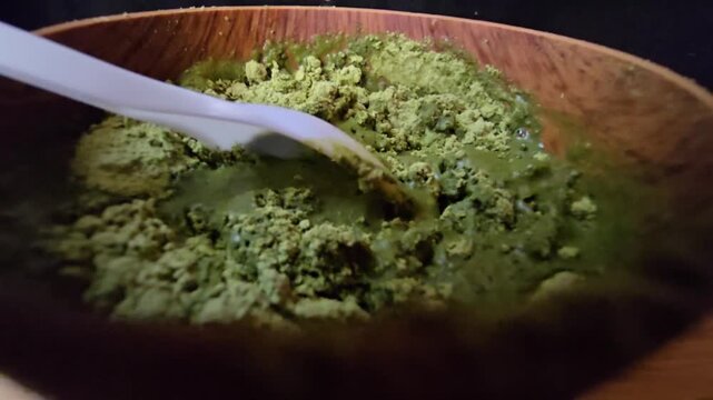 Close-up of mixing Sidr (Ziziphus spina-christi ) herbal powder with water in a wooden bowl, demonstrating the texture of a natural skincare preparation.