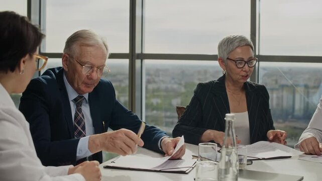 Handheld shot of diverse senior and middle aged business partners and scientists in lab coats signing contract and shaking hands during meeting. Ideal for energy and scientific collaboration videos