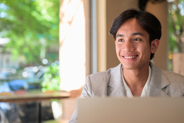 Fototapeta premium Portrait of smiling non-binary Thai Isan professional using laptop