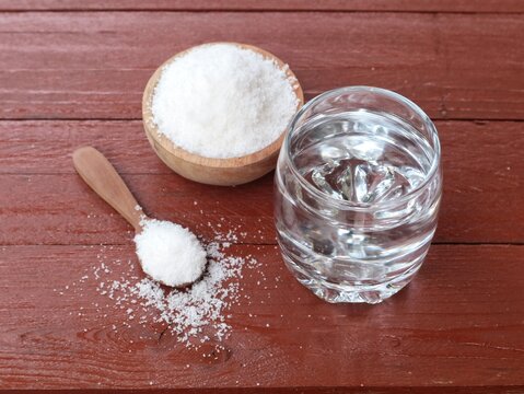 Salt water solution in glass with salt on wooden bowl and spoon on wooden table. Concept for dietary supplements, health drinks, and daily nutrition