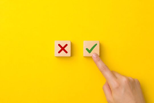 Hand points at a wooden block with a green checkmark while another block with a red cross remains unselected against a bright yellow background.