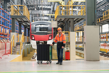 Obraz premium Skilled maintenance worker pushes wheeled cart filled with tools towards large electric train within spacious railway maintenance hall for servicing and repairs.