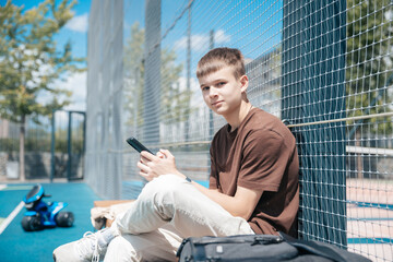 Obraz premium Teenager Enjoying a Sunny Day at the Park While Sitting on a Blue Court and Using His Smartphone With a Toy Nearby