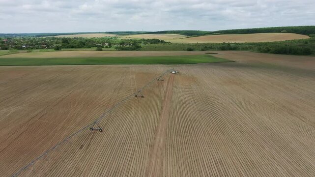 Aerial top view of a green agricultural tractor spraying chemicals, fertilizer, or pesticides on a large farming field with visible rows.