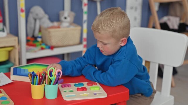 Boy places a wooden puzzle piece into a shape board on a red table inside a building playroom; calm concentration learning.