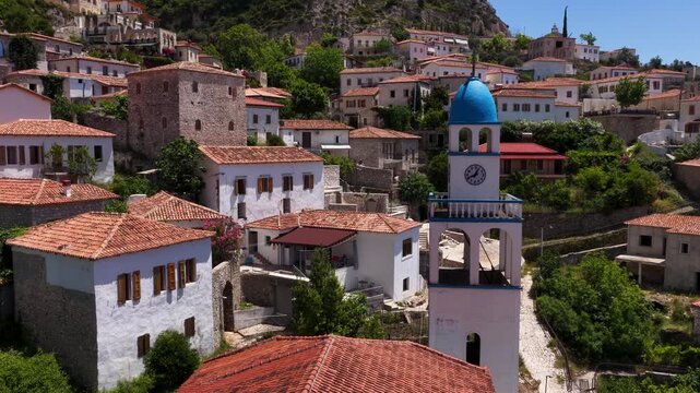 Aerial view of the traditional stone houses with terracotta roofs and a blue domed church tower in the historic village of Dhermi, Vlore County, Albania.