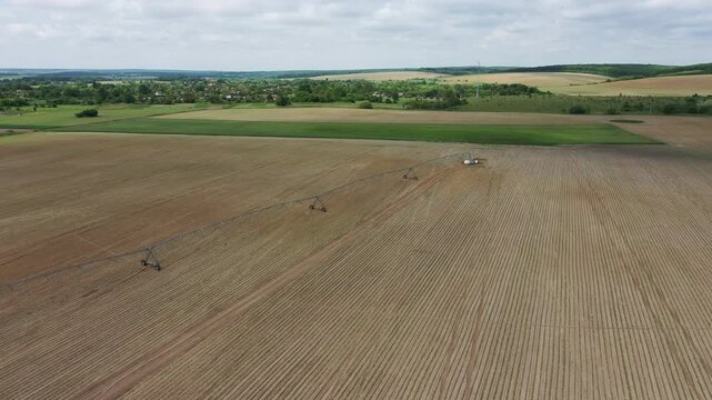Aerial top view of a green agricultural tractor spraying chemicals, fertilizer, or pesticides on a large farming field with visible rows.