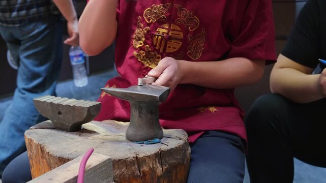 chinese craftsman hammers silver ingot on anvil at tourist market. skilled craftsman shapes metal with traditional tools. watching craftsman work shows ancient heritage and artisan concept today.