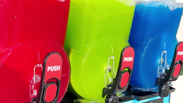 Closeup of generic unbranded commercial icy drinks machines, with bright red, green and blue colored slush textured contents being agitated, ready to deliver on demand semi frozen, sweet beverages.