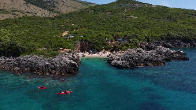 Aerial view of people in red kayaks paddling through the turquoise waters of Aquarium Bay surrounded by rocky cliffs and lush green hills in Himara, Qarku i Vlores, Albania.