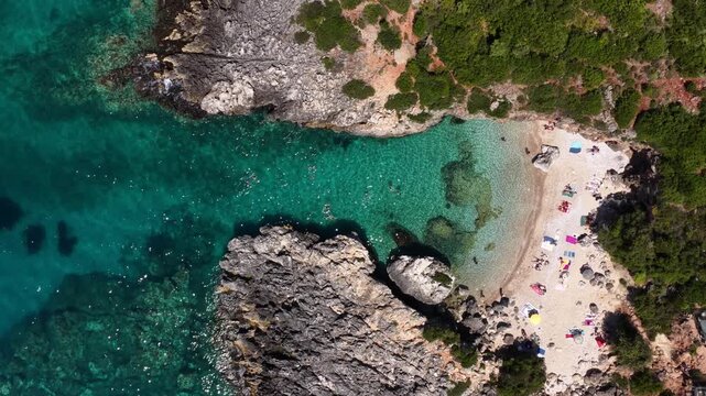 Aerial view of Aquarium Bay with turquoise water and people on the beach in Himara, Qarku i Vlores, Albania.