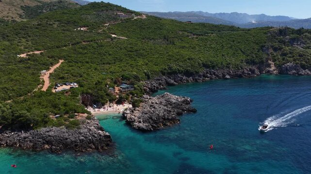 Aerial view of Aquarium Bay featuring turquoise waters, rocky cliffs, and boats along the lush green coastline in Himara, Qarku i Vlores, Albania.