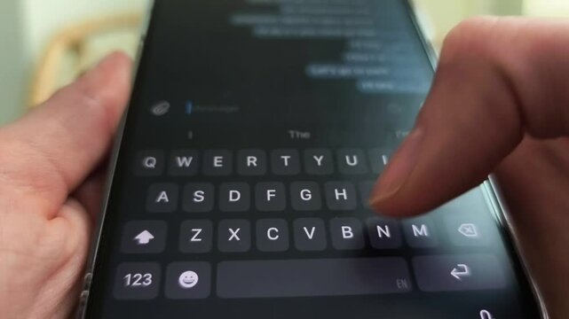 Hands type on a smartphone keyboard in close up. Fingers tap a mobile screen during chat entry. Digital messaging and app communication concept..