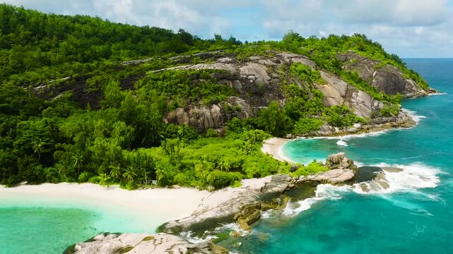 A rocky coastline with turquoise water and dense tropical greenery along the shore. Seychelles, Mahe. Therese.