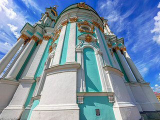 Naklejka premium Low angle view of a beautiful baroque church with turquoise walls and gold decorations under a bright blue sky.
