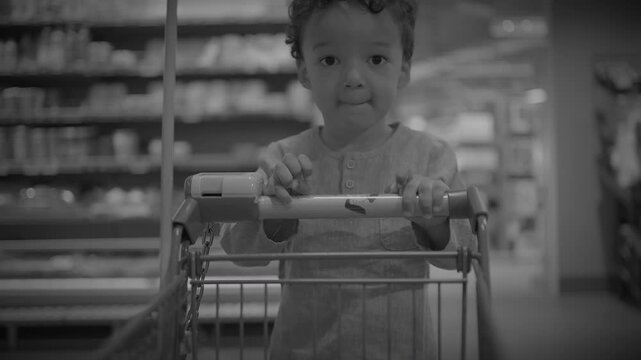 Toddler seated in supermarket shopping cart gripping handle