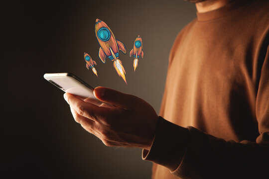 Close-up image of a man in a hoodie holding a smartphone with a rocket drawing on it