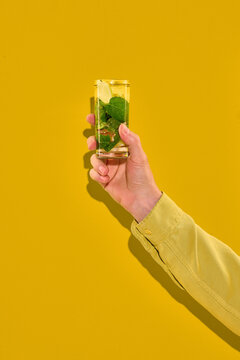 Hand holding mojito cocktail on yellow background with copy space. Concept of summer travel, mocktail market, cocktail menu, beverage ads, and social media content.