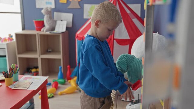 Boy pressing buttons on a toy cash register and exploring an abacus while standing in a toy filled building; concentration learning.