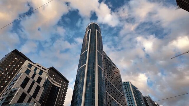 An impressive low-angle view of modern glass skyscrapers and tall buildings in a bustling city, showcasing modern urban architecture against the dramatic, cloudy blue sky of Batumi, Georgia,
