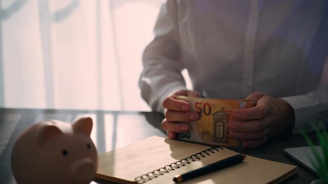 Businesswoman counting euro banknotes and writing financial notes in notebook next to piggy bank, symbolizing savings, investment, and budget planning