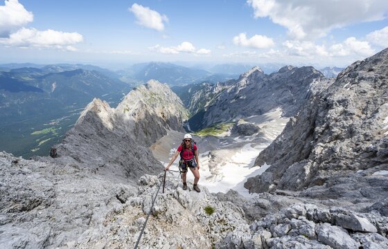 Mountaineer with helmet in a secured via ferrata, Zugspitze via ferrata, ascent to the Zugspitze, view of mountain basin with snow field of the H&ouml;llentalferner and H&ouml;llental, Wetterstein range, Wetterstein range, Bavaria, Germany