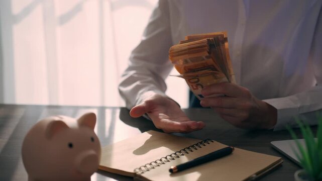 Close up of businesswoman confidently holding and tapping stack of euro banknotes against hand at an office desk. Financial success, profit, income growth and wealth concept.