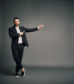 Stylish man in black suit pointing hands at grey copy space