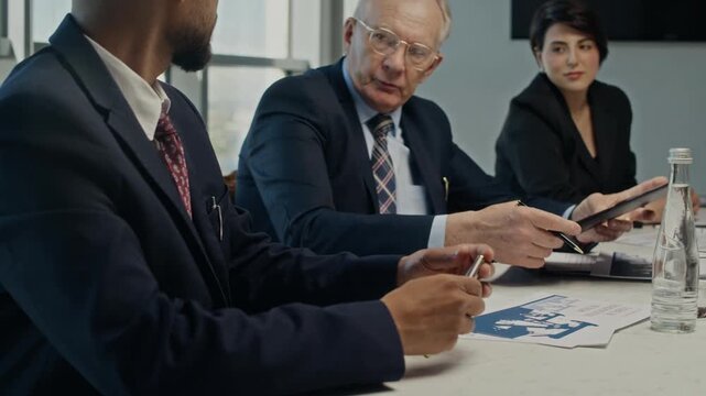 Handheld shot of Indian businessman presenting document to senior Caucasian partner signing contract during oil industry meeting. Ideal for energy sector and corporate law videos