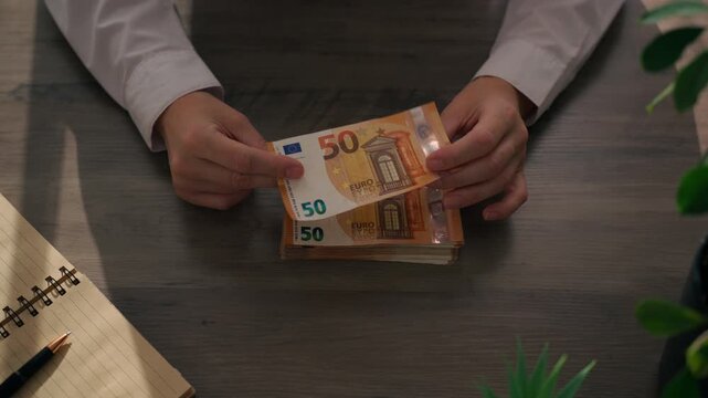 Woman in white shirt sit at office desk without visible face, hold and examining 50 euro banknotes from stack of cash, check authenticity and counting money.Сash handling, finance, money management