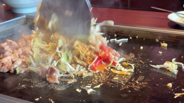 日本のもんじゃ焼き。鉄板焼き料理。カレー味のキャベツや鶏肉をコテで混ぜる動画。