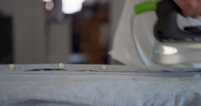 Ironing Clothes: A close-up shot shows a hand holding an iron, pressing it down on a wrinkled shirt laid flat on an ironing board, making it smooth and neat.