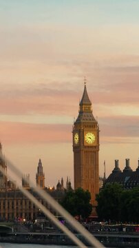 Vertical 4K video of Big Ben and the Houses of Parliament at sunset in London, filmed from a moving train on a bridge, with passing beams intermittently obscuring the iconic skyline