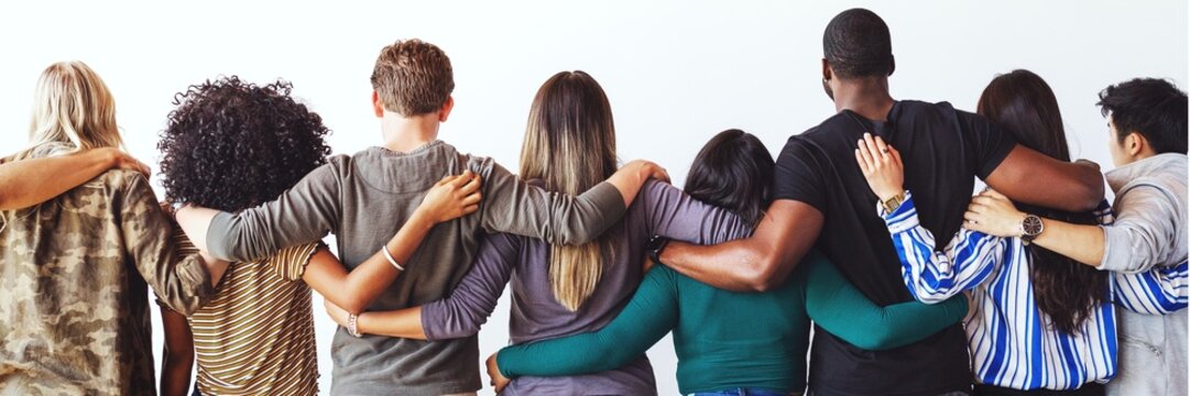 Diverse group of people standing with arms around each other, seen from behind.