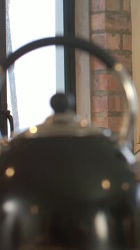 Vertical video: Shifting camera revealing blurred dark kettle at window with brick column and plant