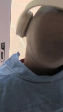 Vertical video: Pointing denim-clad man with headphones at patio door, adjusting pull cord to open
