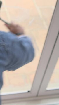 Vertical video: Starting hand gripping squeegee and cleaning sliding door, man in denim shirt, hat