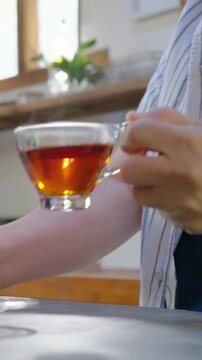 Vertical video: Holding phone on table red-nailed hands lifting cup onto saucer, showing teapot