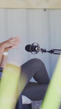 Vertical video: Recording starting, woman leaning back gesturing and speaking in nook, mic, plant