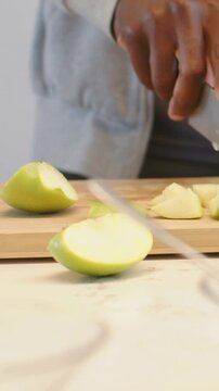 Vertical video: Entering right hand, slicing half green apple for snack on wood board, knife